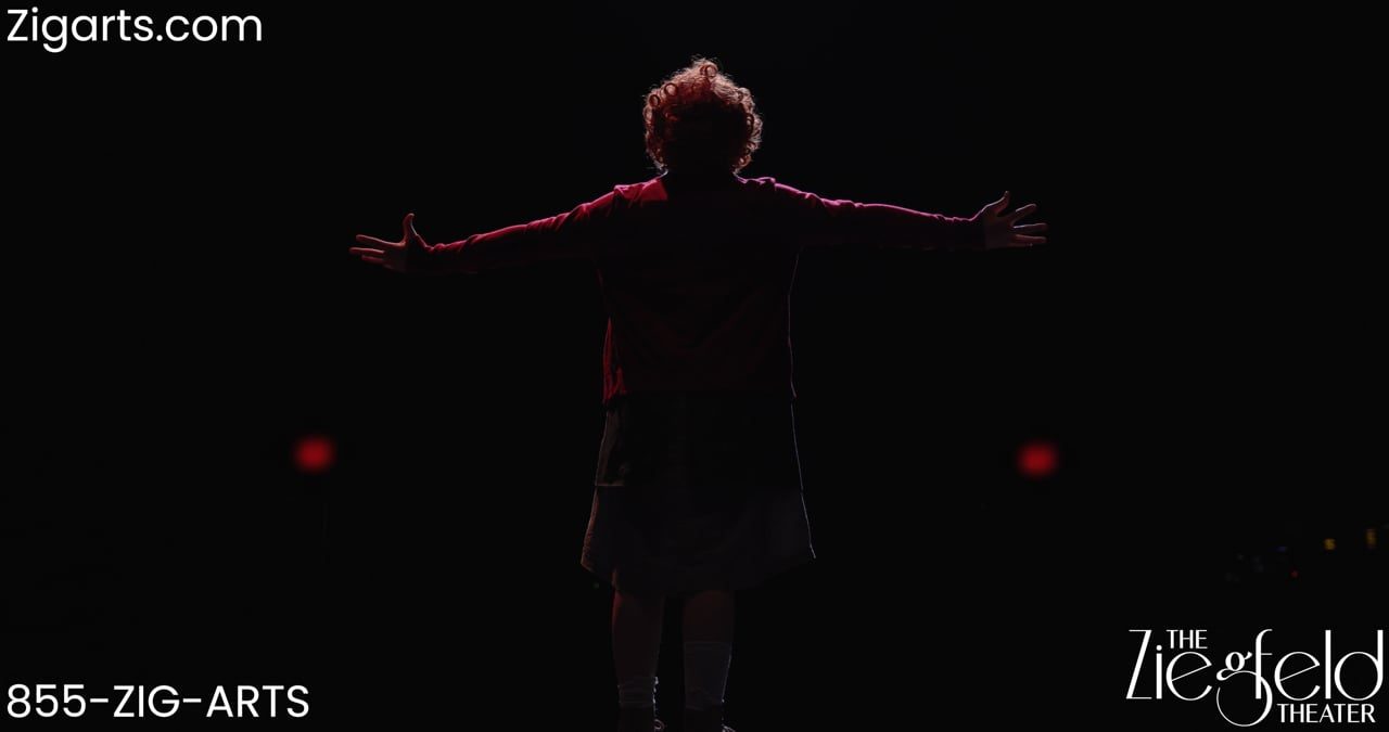 A performer with arms outstretched on a dark stage