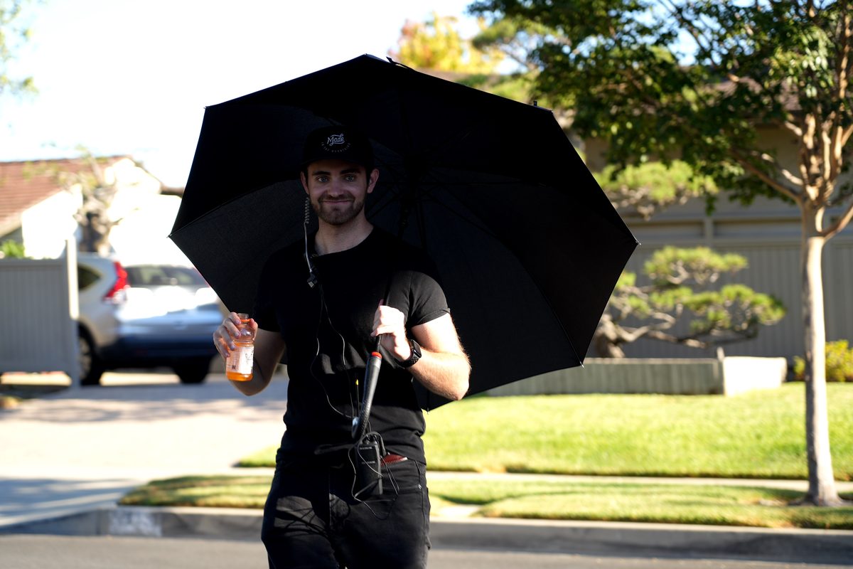 Smiling under a black umbrella between takes on location