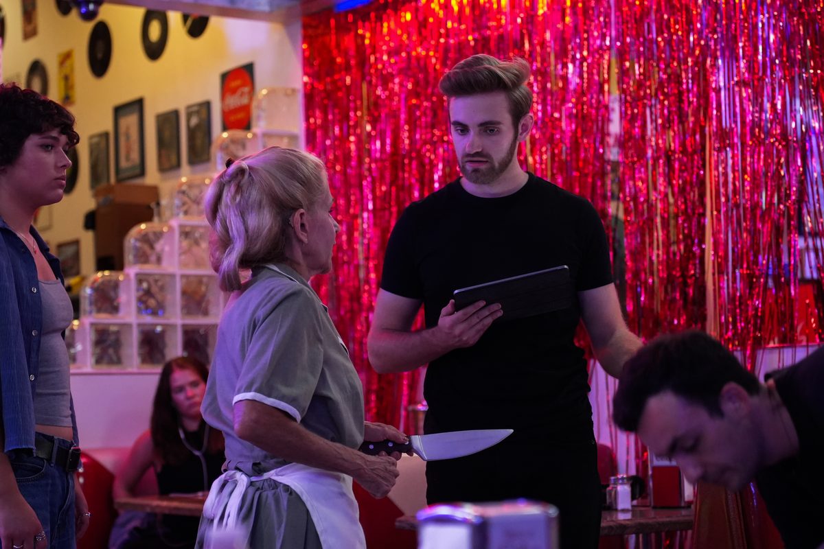 Directing actors on a diner set, script tablet in hand