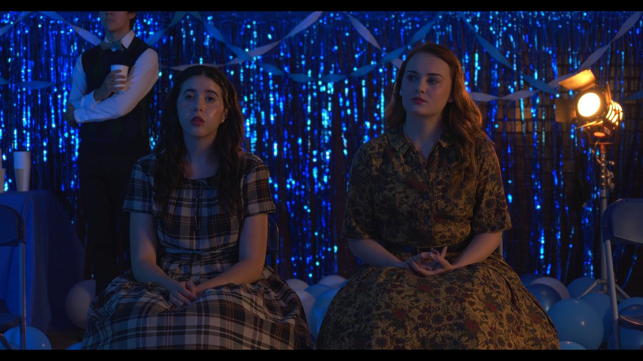 Two young women in plaid sit against a blue tinsel backdrop