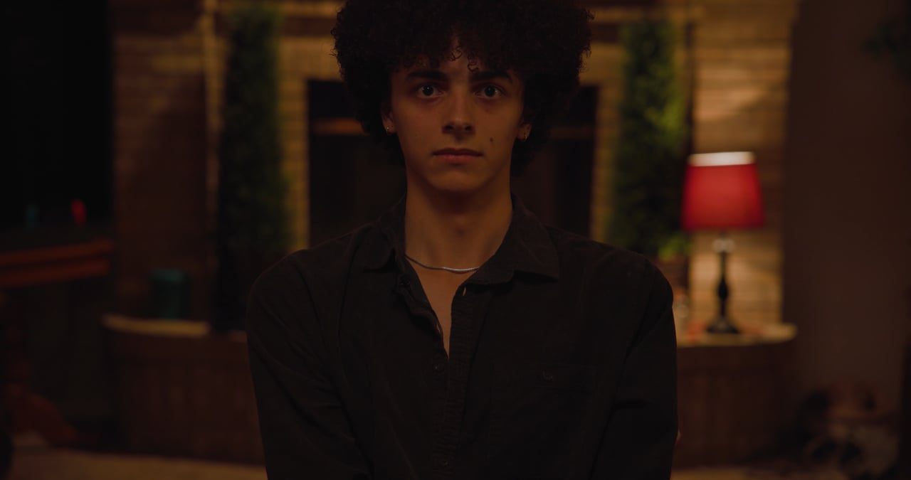 A young man stands in a dim, warm-lit room